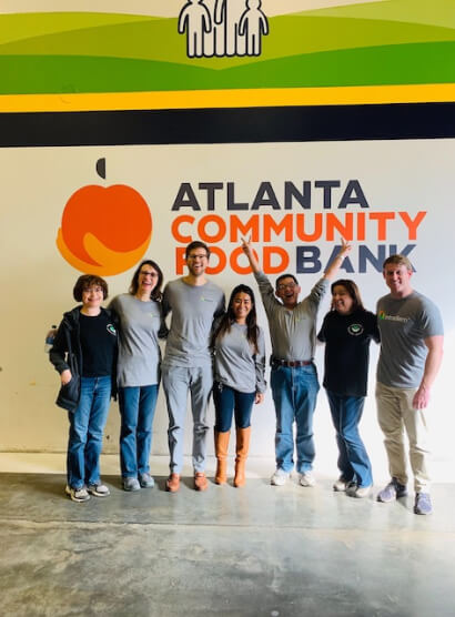 Group of Intradiem employees smiling in front of Atlanta Community Food Bank sign showcasing our culture of service