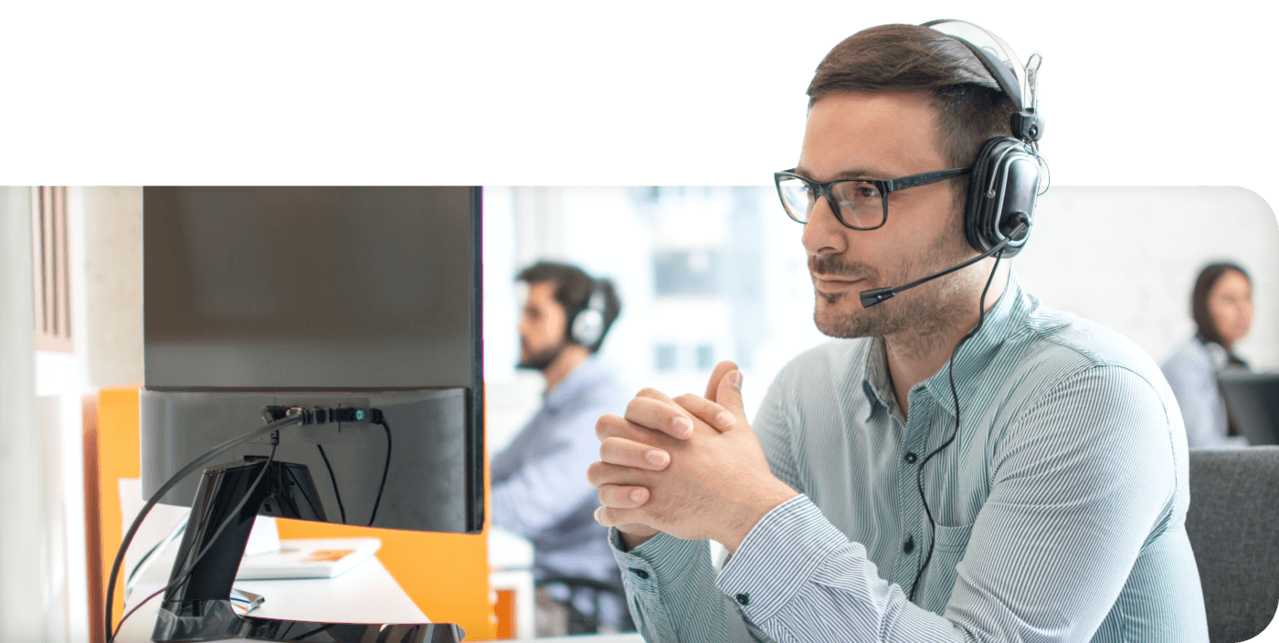 Intradiem support employee with headset on looking at computer with support team in the background