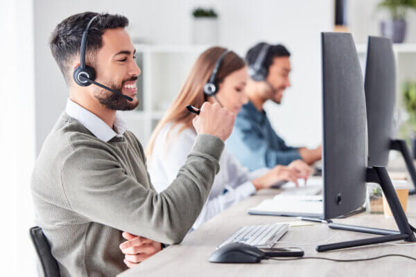 Contact center team of 3 people wearing headsets smiling looking at their computers